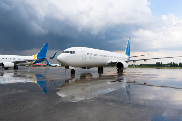 Two airplanes parked on a wet airport under a cloudy sky
