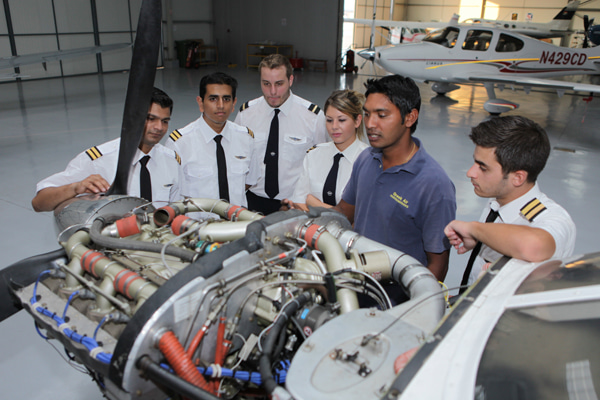 Students in pilot uniforms and an instructor around engine