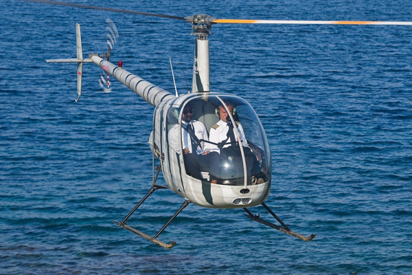 Two-seat helicopter flying above blue water